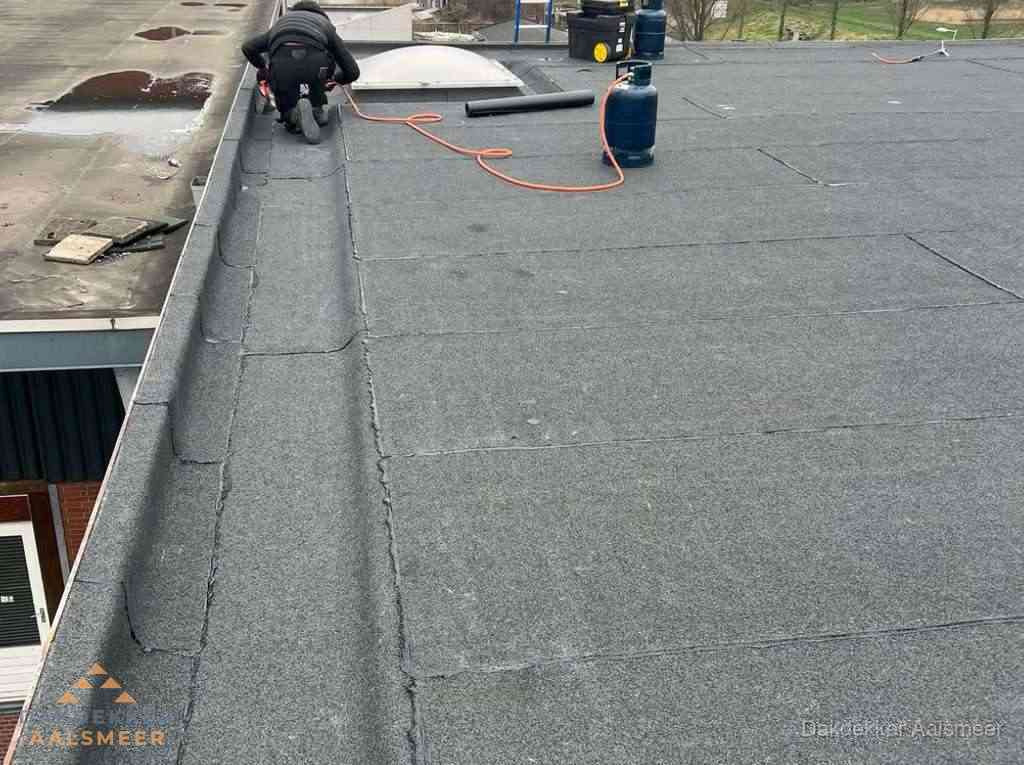 Dakdekker repareert bitumen dakbedekking op groot plat dak in Aalsmeer